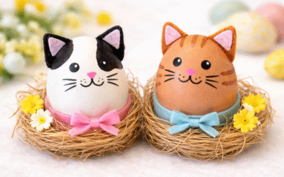 Dwa wielkanocne jajka stylizowane na koty – biało-czarny i rudy – umieszczone w małych gniazdkach ze słomy, ozdobione pastelowymi kokardkami i kwiatami na jasnym tle.
